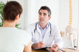 Male Doctor writing something down while patient is talking in a room