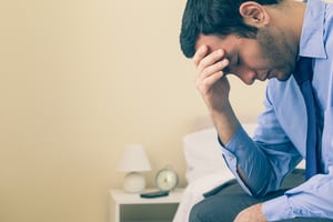 Sad man sitting head in hands on his bed in a bedroom at home