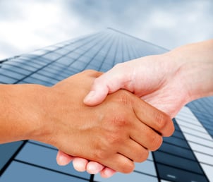 Close up of a business handshake with an office building behind.jpeg