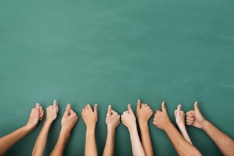 Close up view of the hands of a group of people giving a thumbs up gesture of approval an success with their hands raised against a blank green chalkboard with copyspace.jpeg