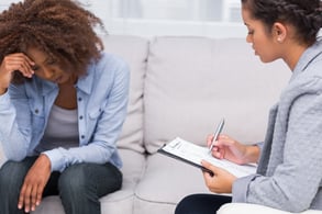 Woman sitting on sofa at therapy with doctor taking notes