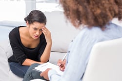 Woman crying on sofa during therapy session while therapist is taking notes